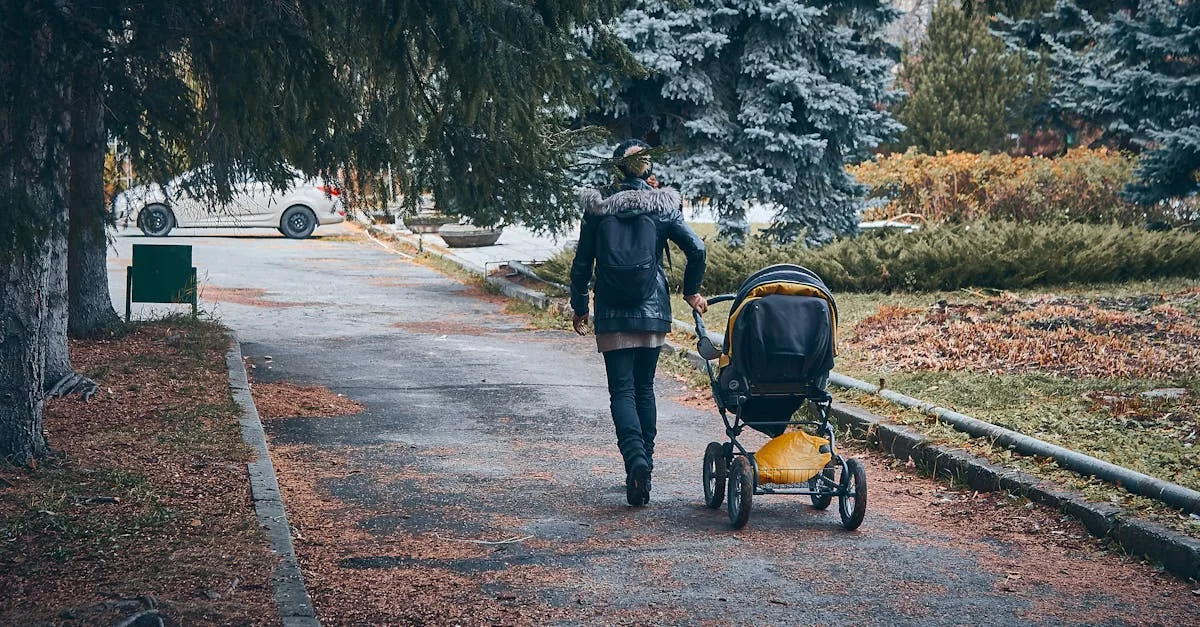 A mother pushes a stroller with her child while talking on the phone on a sunny city sidewalk.