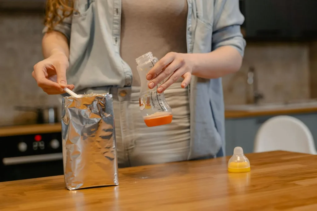 Parent preparing baby bottle with formula on a kitchen counter