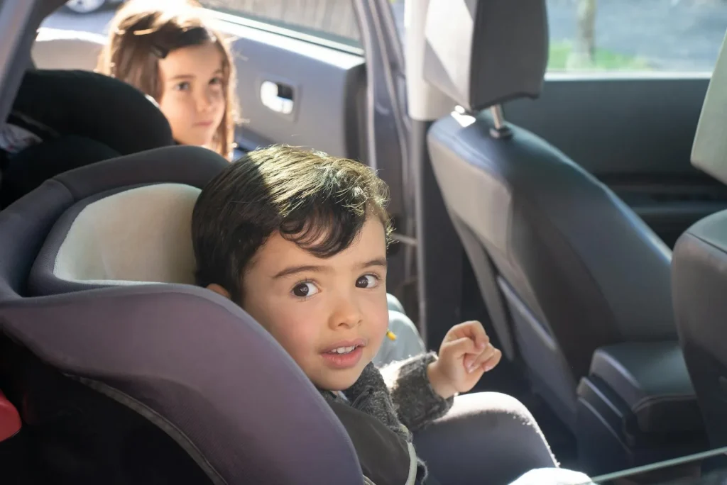 Two children securely strapped into car seats in the back seat of a family car