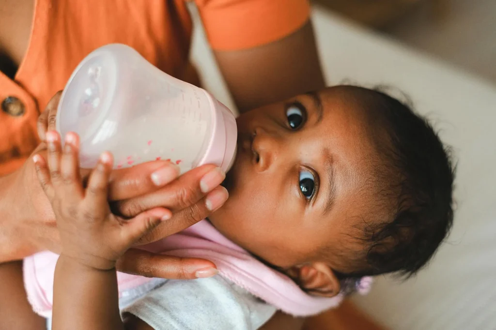 Parent bottle feeding a baby with warm milk