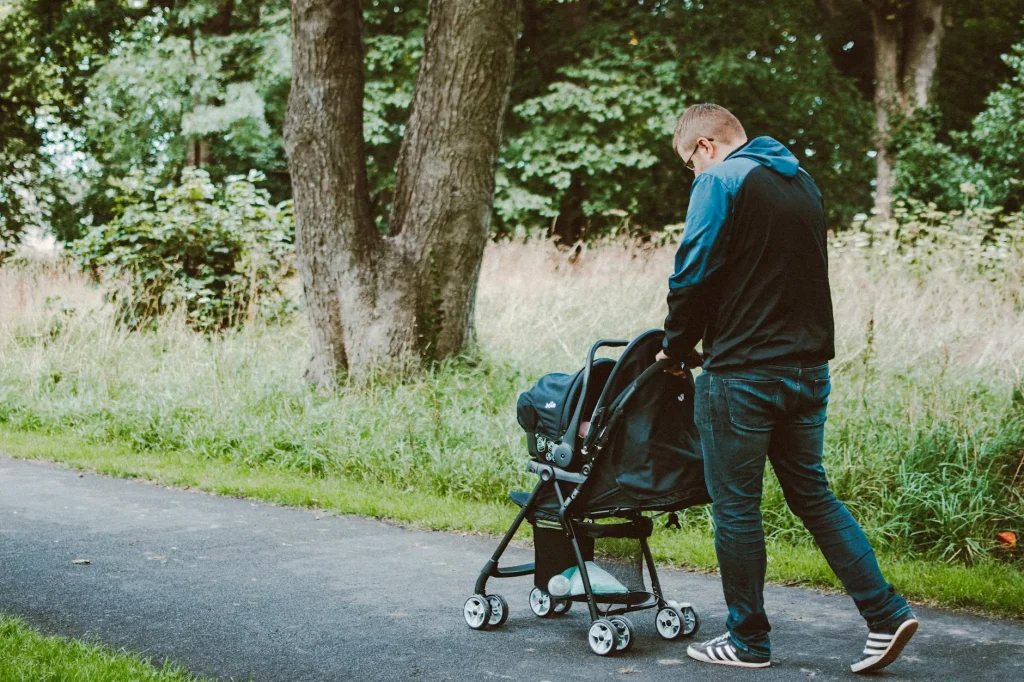 Parent pushing a pushchair along a park path with their baby