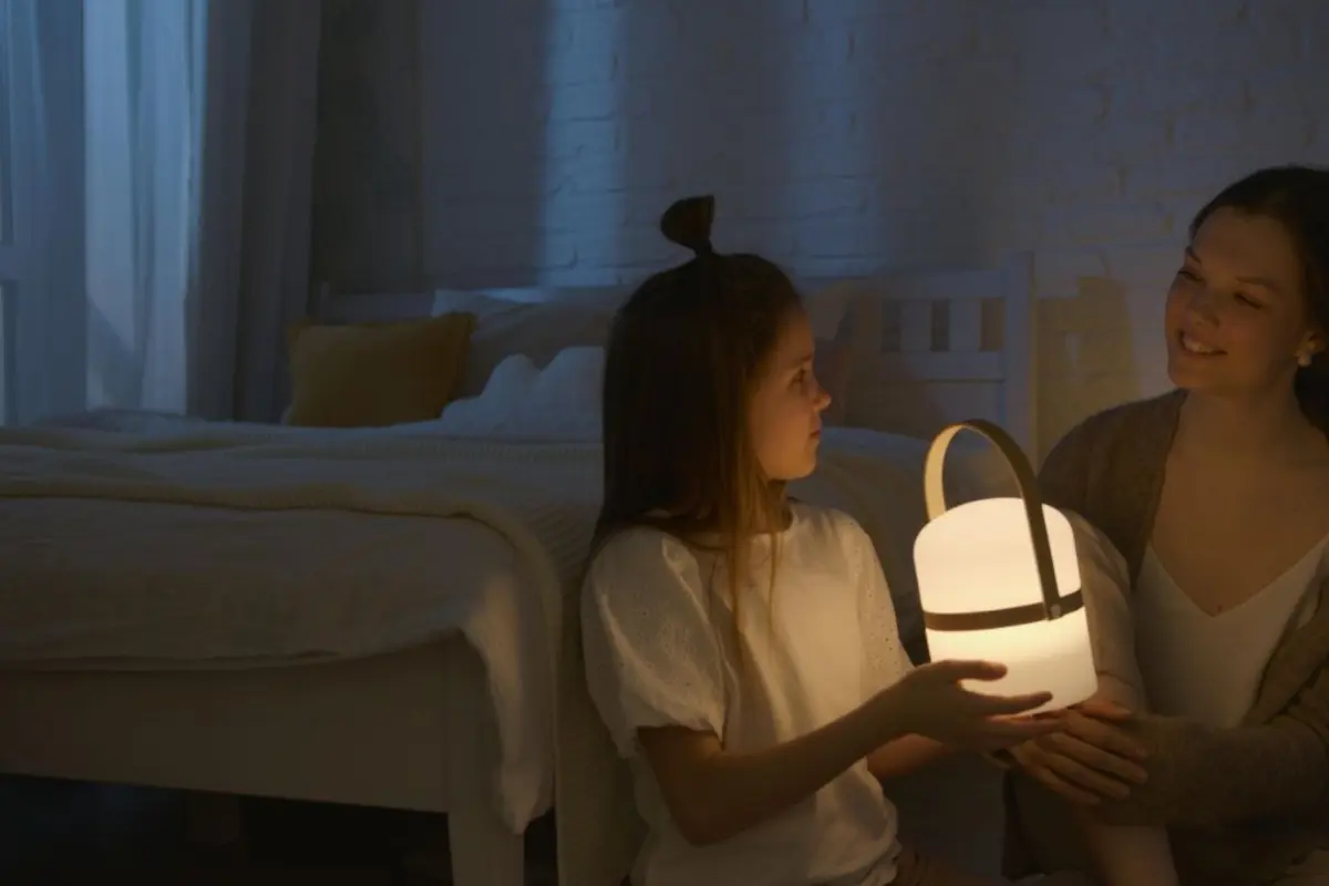 Mother and child holding a portable night light in a dimly lit bedroom