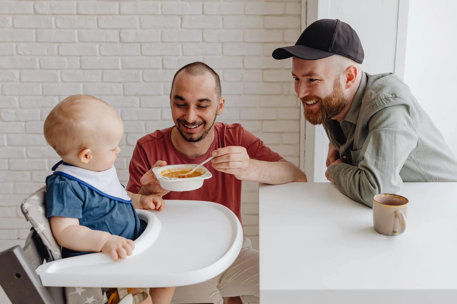 Parent offering puree on a spoon to a baby in a highchair